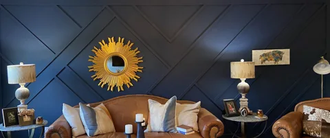 A deep blue wall with intersecting diagonal trim, a gold sunburst mirror, and leather seating.