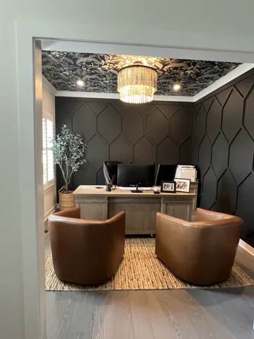 Dark geometric wall panels frame a desk beneath a patterned ceiling.