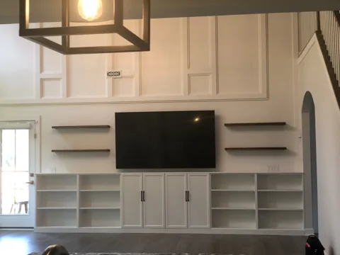 White rectangular wall panels rise above a television and open shelving.