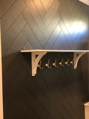 Overlapping diagonal trim creates a dark backdrop for a shelf and coat hooks.