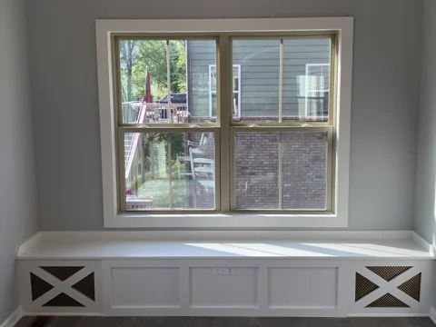 A white built-in window bench has paneled doors and crossed end details.