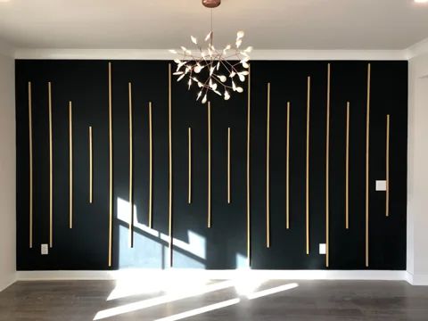 Slim gold-colored vertical accents of different lengths stand against a dark wall.