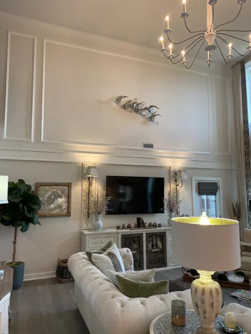 Large white rectangular wall panels rise above a fireplace in a tall living room.