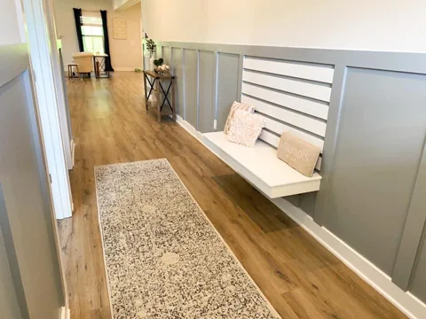 A built-in white bench with horizontal wall boards sits along a paneled hallway.