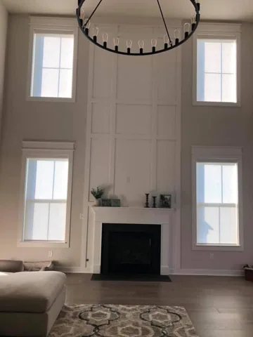 White vertical wall trim rises around a fireplace between tall windows.