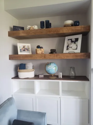 Wood floating shelves sit above white storage cabinetry in a work area.