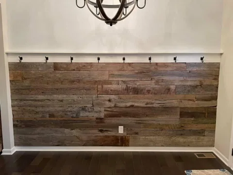 Varied wood planks fill an entry wall beneath a row of dark coat hooks.