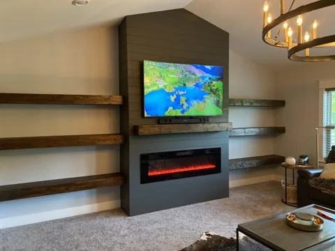 A dark fireplace and television are paired with long floating wood shelves.