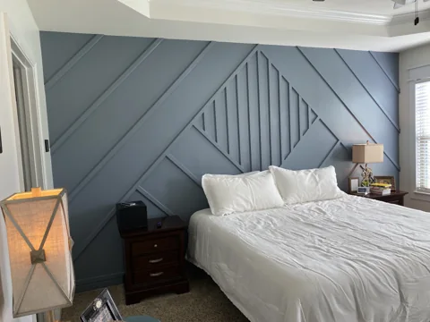 Diagonal trim and a central vertical pattern frame a bed on a blue-gray wall.