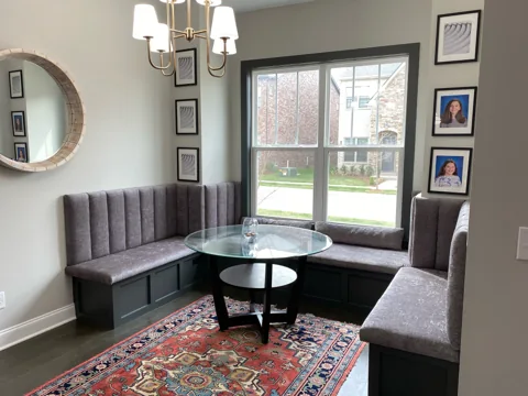 An upholstered corner banquette sits beneath windows around a round dining table.