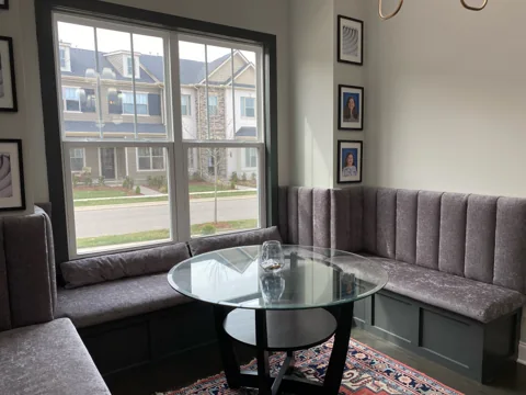 A cushioned window-side bench sits beside a round black table.