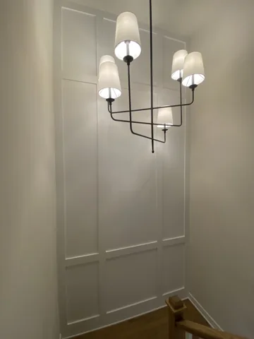 White picture-frame molding follows a stairwell below hanging lights.