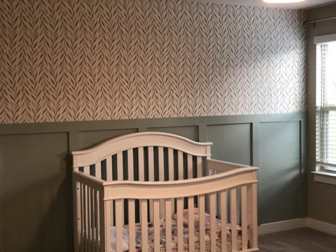 Green lower wall panels meet patterned wallpaper behind a crib.