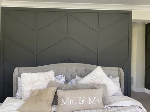 Muted green angled trim creates a geometric feature wall behind a bed.