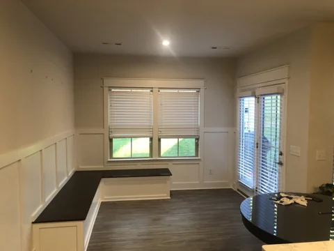A built-in corner bench with gray cushions sits beneath a wide window.