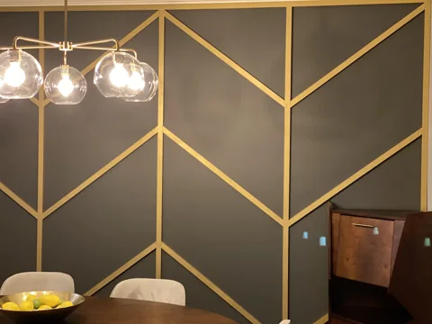 Gold-colored diagonal trim forms a repeating angular pattern in a dark dining room.