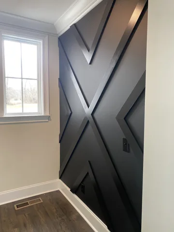 Bold dark diagonal wall panels meet beside a narrow window.