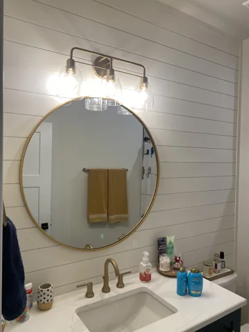 White horizontal wall boards sit behind a round bathroom mirror.