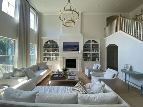 Arched white bookcases flank a paneled fireplace in a bright living room.