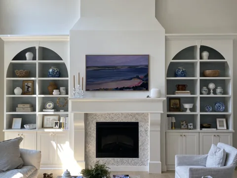 A closer view shows white arched bookshelves beside a fireplace and television.