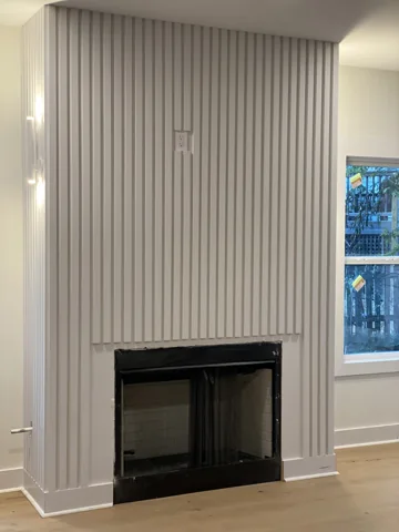 Narrow vertical slats surround a dark fireplace beside a window.