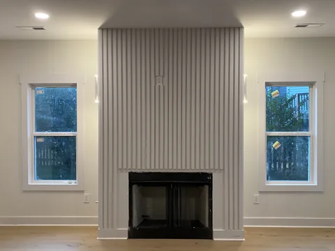 Vertical slats cover a fireplace wall between two windows.