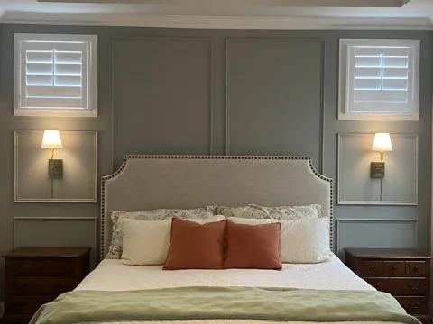 Gray wall panels frame a bed, with sconces set between shutters.