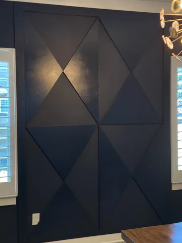 A dark feature wall has large triangular panels with subtle changes in sheen.