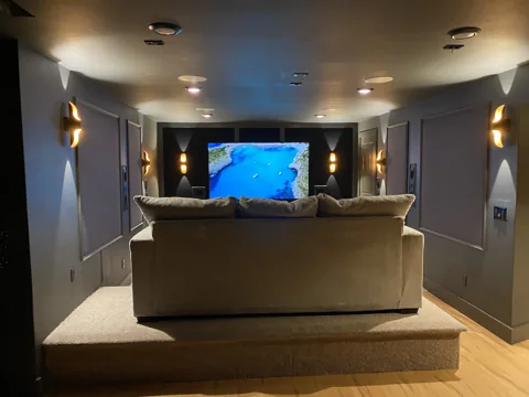 Geometric wall panels frame a screen in a room with curved seating.