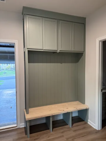 A light-colored entry unit combines upper cabinets, a wood bench, and lower cubbies.